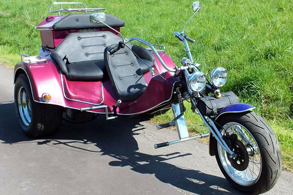 Ein dreirädriges Motorrad mit Beiwagen, ausgestattet mit zwei Scheinwerfern und einem auffälligen Vorderrad, bereit für die Beförderung von Passagieren oder Fracht.