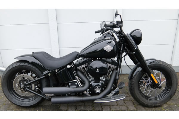Schwarzes Harley Davidson Motorrad auf einer gepflasterten Oberfläche vor einer weißen Wand geparkt.