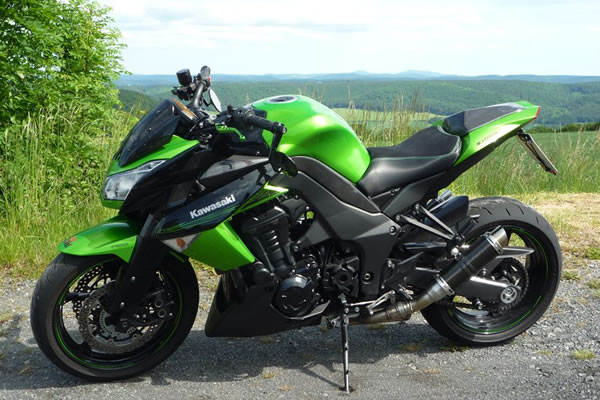 Grünes und schwarzes Kawasaki Sportmotorrad auf einer Asphaltfläche mit einer natürlichen Landschaft im Hintergrund geparkt.