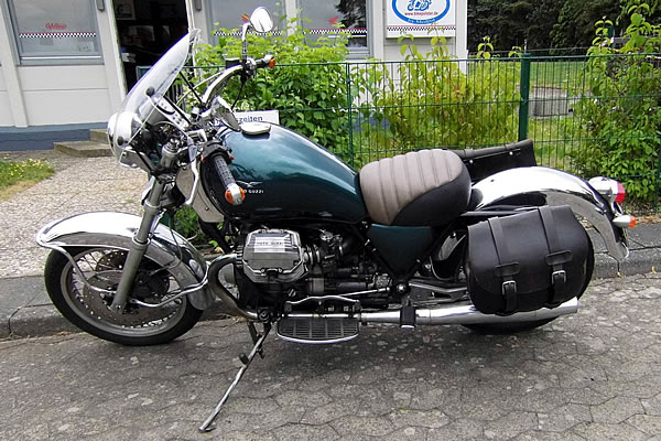 Moto Guzzi Motorrad mit dunkelgrünem Kraftstofftank und weißen Details auf einer gepflasterten Oberfläche geparkt.
